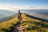 Hiker standing on a mountain ridge above alpine meadows with wildflowers, looking out over the Okanagan valley from Big White Mountain.