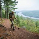 Hiker ascending a forest trail on Mont Rigaud with distant views toward the Ottawa River valley.
